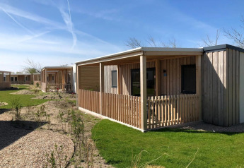Außenaufnahme von Holzhütten der Cosy Unique Lodge mit Veranden, grünen Rasenflächen und blauem Himmel.