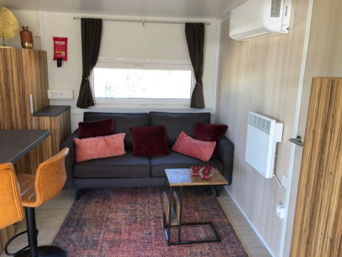 Moderne og hyggelig stue i Cosy Unique-lodge på EuroParcs Veluwemeer, med sofa, puder og vindue.