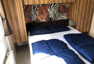 Camera da letto con letto matrimoniale, biancheria blu e arte murale animale al Cosy Unique, EuroParcs Veluwemeer, Paesi Bassi.