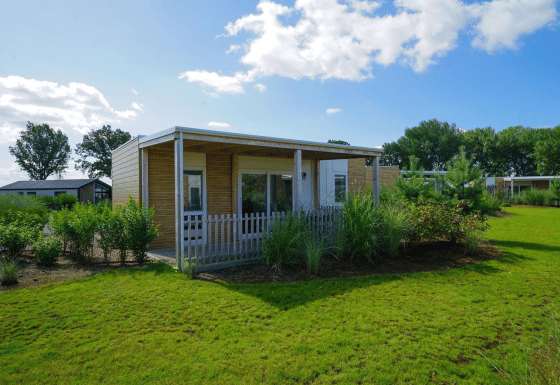 Un lodge moderno y acogedor llamado Cosy Unique, rodeado de césped verde y árboles, bajo un cielo soleado.