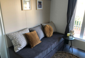 Zona giorno nel lodge Cosy Unique a EuroParcs Veluwemeer con divano grigio, cuscini e tavolino.