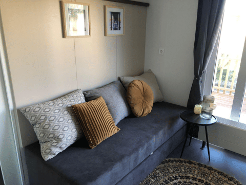 Zona giorno nel lodge Cosy Unique a EuroParcs Veluwemeer con divano grigio, cuscini e tavolino.