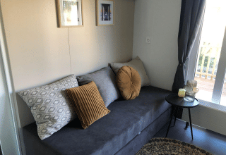 Sala en el lodge Cosy Unique de EuroParcs Veluwemeer con sofá gris, cojines y mesa auxiliar redonda.