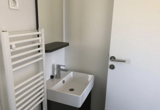 Lille badeværelse på Cosy Unique, EuroParcs Veluwemeer, Holland, med vask, hvid dør og radiator.