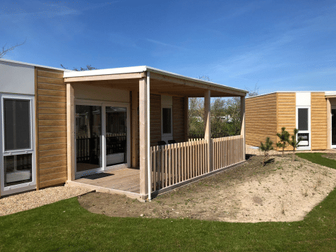 Buitenaanzicht van de Cosy Unique lodge bij EuroParcs Veluwemeer in Nederland met houten terras en hek.