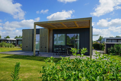 Moderne Domus-lodge met houten buitenzijde, ruim terras, tuintafel en zicht op een groene tuin.