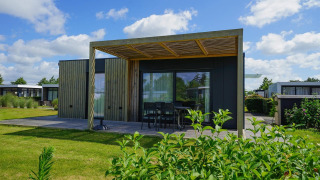 Moderne Domus-lodge met houten buitenzijde, ruim terras, tuintafel en zicht op een groene tuin.