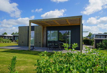 Moderne Domus-lodge met houten buitenzijde, ruim terras, tuintafel en zicht op een groene tuin.