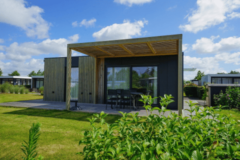 Lodge Domus moderno con fachada de madera, terraza amplia, muebles de exterior y jardín verde exuberante.
