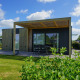 Moderne Domus-lodge met houten buitenzijde, ruim terras, tuintafel en zicht op een groene tuin.