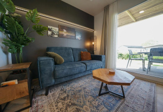 Moderne woonkamer in Domus-lodge bij EuroParcs Veluwemeer, Nederland, met blauwe zetel en houten tafel.