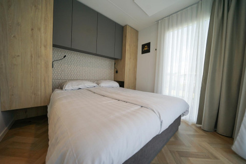 Modernes Schlafzimmer mit Doppelbett, Vorhängen und Holzboden in Domus im EuroParcs Veluwemeer, Niederlande.