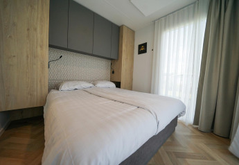Moderne slaapkamer met tweepersoonsbed, lichte gordijnen en houten vloer in Domus van EuroParcs Veluwemeer.