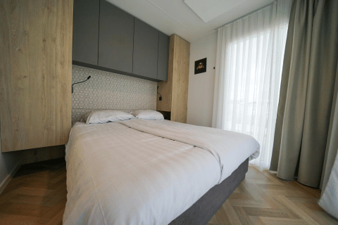 Dormitorio moderno con cama doble, cortinas claras y suelo de madera en Domus de EuroParcs Veluwemeer, Países Bajos.