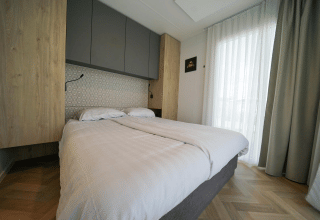 Dormitorio moderno con cama doble, cortinas claras y suelo de madera en Domus de EuroParcs Veluwemeer, Países Bajos.