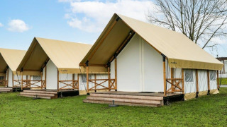 Tentes safari glamping à toits beiges et terrasses en bois, dressées sur pelouse sous ciel bleu.