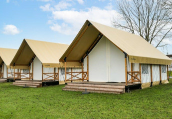 Safari-Glampingzelte mit Holzveranda und beigen Planendächern auf einer Wiese unter blauem Himmel.