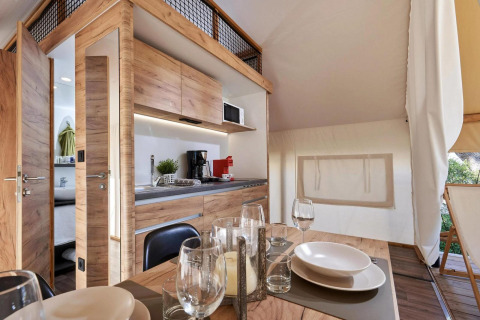 Hébergement glamping moderne au décor bois, cuisine entièrement équipée et coin repas confortable.