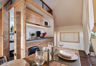Hébergement glamping moderne au décor bois, cuisine entièrement équipée et coin repas confortable.