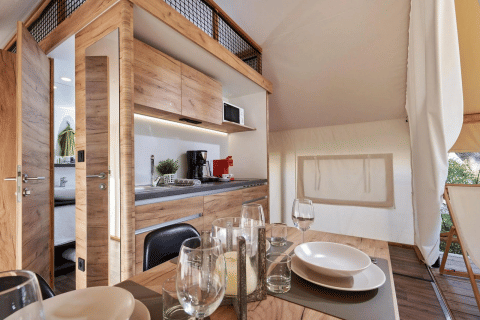 Moderne glamping-accommodatie met houten interieur, volledig uitgeruste keuken en eethoek.