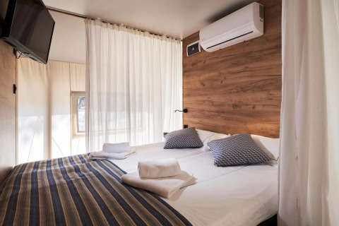 Chambre de tente glamping moderne avec lit double, climatisation, TV murale et mur à accents bois.