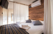 Modernes Glampingzelt mit gemütlichem Doppelbett, Klimaanlage, TV und Holzakzentwand im Schlafzimmer.