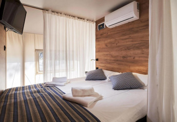 Chambre de tente glamping moderne avec lit double, climatisation, TV murale et mur à accents bois.