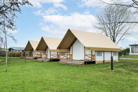Drie glamping safaritenten op een groen grasveld met houten veranda’s en omliggende moderne faciliteiten.