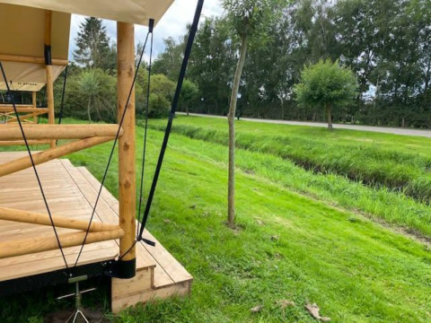 Terraza de madera de una tienda safari en EuroParcs Veluwemeer, Países Bajos, con césped y árboles verdes.