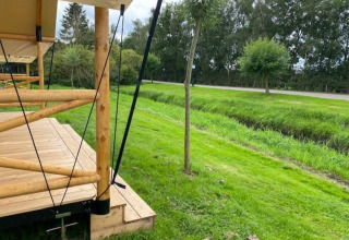 Terraza de madera de una tienda safari en EuroParcs Veluwemeer, Países Bajos, con césped y árboles verdes.