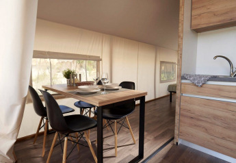 Eethoek met modern houten tafel en zwarte stoelen in een glamping tent met keuken en veel daglicht.
