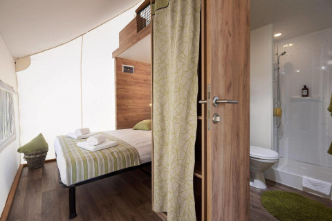 Interno di una tenda safari con letto matrimoniale, bagno privato e arredo moderno in legno.