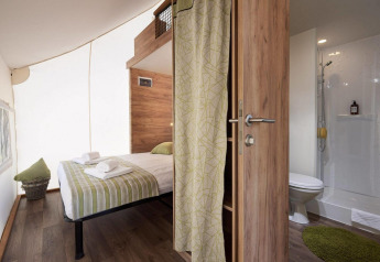 Interno di una tenda safari con letto matrimoniale, bagno privato e arredo moderno in legno.