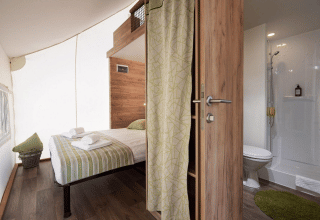 Innenansicht eines Safarizeltes mit Doppelbett, Badezimmer, moderner Holzverkleidung und Dusche.