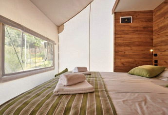 Gemütlicher Schlafbereich im Glampingtent mit Doppelbett, Holzverkleidung und Blick ins Grüne.