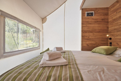 Indretning af soveområde i Glampingtent med dobbeltseng, træpaneler og udsigt til naturen udenfor.