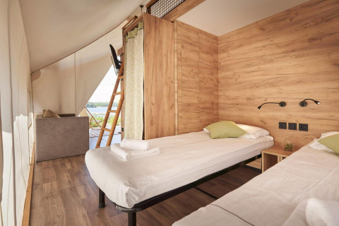 Interior view of a safari tent bedroom with two single beds, wood paneling, and a scenic outdoor view.