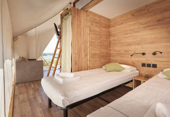 Chambre intérieure d’une tente safari avec deux lits simples, murs en bois clair et vue sur l’extérieur.