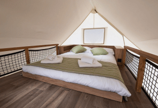 Interno di una tenda glamping di lusso con letto matrimoniale, cuscini verdi e pavimento in legno.
