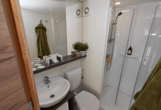 Salle de bain moderne et compacte dans un hébergement glamping avec douche, WC, lavabo et serviettes vertes.