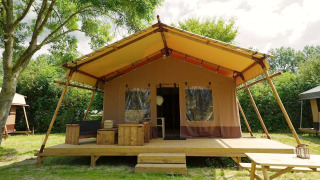 Glampingtent Desert with wooden deck, patio furniture, and a spacious veranda surrounded by greenery.