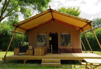 Glampingtent Desert sur terrasse en bois, mobilier extérieur, grande véranda dans un cadre verdoyant.