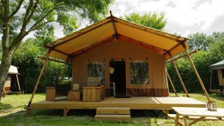 Glampingtent Desert con veranda spaziosa, pedana in legno e mobili da esterno immerso nel verde.