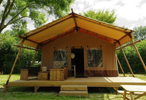 Glampingtent Desert sur terrasse en bois, mobilier extérieur, grande véranda dans un cadre verdoyant.