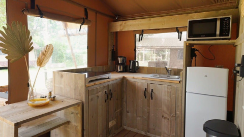 Moderne Glampingküche aus Holz mit Kühlschrank, Mikrowelle und Fenstern, Glampingtent Desert, tagsüber.