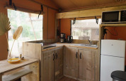 Modern wooden glamping kitchen with fridge, microwave, window views and sunlight at Glampingtent Desert.