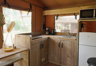 Moderne houten glampingkeuken met koelkast, microgolf en ramen bij Glampingtent Desert overdag.