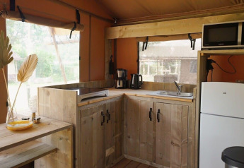 Moderne Glampingküche aus Holz mit Kühlschrank, Mikrowelle und Fenstern, Glampingtent Desert, tagsüber.