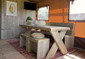 Interior of Glampingtent Desert showing wooden table, benches, colorful rug, and orange window coverings.