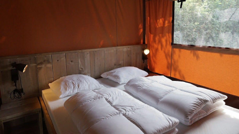 Schlafbereich im Glampingtent Desert mit Doppelbett, rustikalem Holz und orangefarbenen Vorhängen.